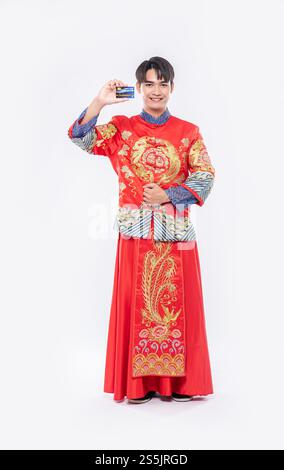 Ein Mann, der einen Cheongsam trägt, hält eine Kreditkarte, um während des chinesischen Neujahrs einkaufen zu gehen. Stockfoto