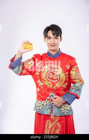 Ein Mann, der einen Cheongsam trägt, hält eine Kreditkarte, um während des chinesischen Neujahrs einkaufen zu gehen. Stockfoto
