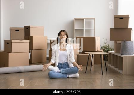Junge Frau, die meditiert, sitzt am Umzugstag auf dem Boden Stockfoto