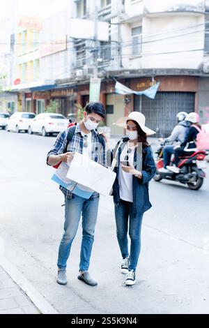 Das junge Backpacker-Paar in Gesichtsmaske, das Papier hält Karte auf der Suche nach der Standortrichtung auf der City Street, hübsche Frauen tragen Sombrero, das sind sie Stockfoto
