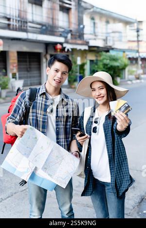 Ein junger Rucksackreisender, der eine Karte in Papierform hält, und eine hübsche Frau trägt einen Sombrero, hält ein Smartphone und zeigt eine Kreditkarte in der Hand, sie benutzen sie, um zu bezahlen Stockfoto