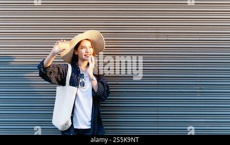 Selektiver Fokus junge Backpackerin weiblich im Sombrero lächelnd, während sie Smartphone hält und Kreditkarte in den Händen hält Stockfoto