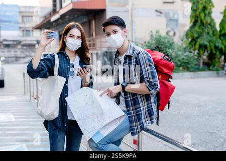 Ein junger Rucksackreisender, der eine Karte in Papierform hält, und eine hübsche Frau trägt einen Sombrero, hält ein Smartphone und zeigt eine Kreditkarte in der Hand, sie benutzen sie, um zu bezahlen Stockfoto