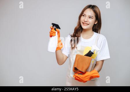 Portrait der jungen asiatischen Frau in Schürze und Gummihandschuhen, Lächeln und Putzgeräte in der Hand halten, Kopierraum Stockfoto