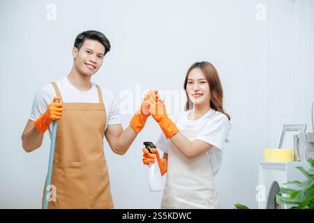Porträt glückliches, lächelndes junges Paar mit Ausrüstung für das Putzhaus, sie tragen Gummihandschuhe, hübsche Frau hält die Spary Flasche in der Hand, sie lächeln Stockfoto
