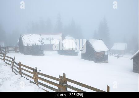 Holzblockhütten in nebeliger Schneelandschaft im Skigebiet und Kurort Băile Harghita (Ungarisch Hargitafürdő), Rumänien Stockfoto