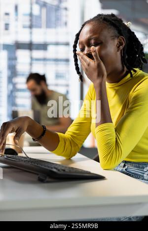 Mitarbeiter im Büro gähnt während der Arbeitsschicht und fühlt sich müde, während sie Online-Geschäftsdokumente durchsehen. Erschöpfter Firmenmitarbeiter, der am Arbeitsplatz schläfrig ist und Aufgaben erledigt Stockfoto