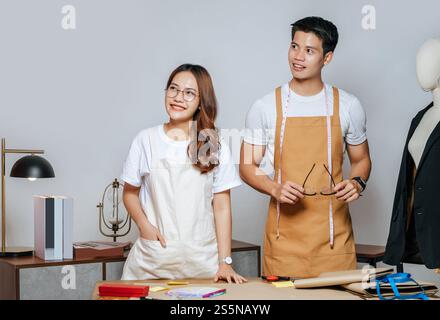 Porträt junger gutaussehender Mann und hübsche Frau in Brille mit Schürze, Paar Modedesigner, die mit Happy, Schaufensterpuppe und Schneiderei zusammenarbeiten Stockfoto