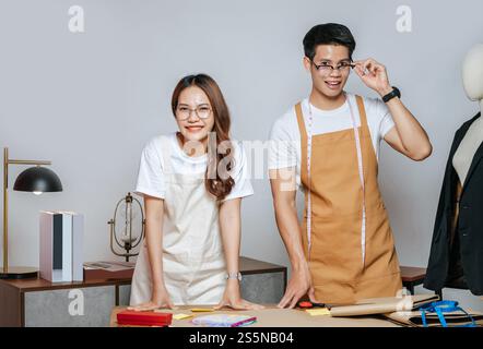 Porträt junger gutaussehender Mann und hübsche Frau in Brille mit Schürze, Paar Modedesigner, die mit Happy, Schaufensterpuppe und Schneiderei zusammenarbeiten Stockfoto