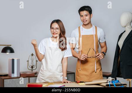 Porträt junger gutaussehender Mann und hübsche Frau in Brille mit Schürze, Paar Modedesigner, die mit Happy, Schaufensterpuppe und Schneiderei zusammenarbeiten Stockfoto
