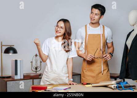 Porträt junger gutaussehender Mann und hübsche Frau in Brille mit Schürze, Paar Modedesigner, die mit Happy, Schaufensterpuppe und Schneiderei zusammenarbeiten Stockfoto