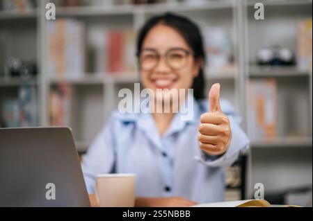 Nahaufnahme und selektiver Fokus auf der Hand einer jungen Frau, die hinter einem Laptop sitzt, heben Sie die Hand hoch mit aufgeblasenen Likes und Lächeln Stockfoto