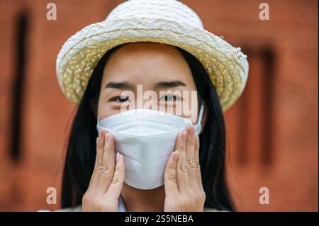 Junge asiatische Backpackerin, die Hut und Schutzmaske trägt, während sie durch die historische Stätte reist, benutzt sie Kamera, um ein Foto mit Happy zu machen Stockfoto