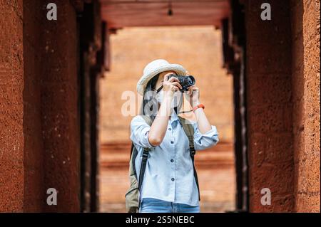 Junge asiatische Backpackerin, die Hut und Schutzmaske trägt, während sie durch die historische Stätte reist, benutzt sie Kamera, um ein Foto mit Happy zu machen Stockfoto