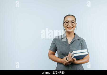 Porträt einer asiatischen Frauenbrille, die Bücher in der Hand hält und im Studio mit Kopierraum über dem Hintergrund steht. Frau, die in die Kamera schaut. Stockfoto