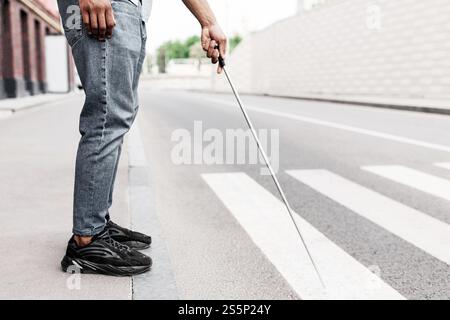 Beschnittene Ansicht eines jungen schwarzen Mannes mit Sehbehinderung, der am Straßenrand steht, mit Gehstock im Stadtzentrum, Platz kopieren Stockfoto