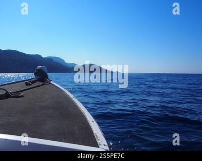 Ein kleines Boot, das durch das tiefblaue Wasser des Ionischen Meeres in Richtung Hügel und des klaren, blauen Himmels in Korfu, Griechenland, fährt Stockfoto