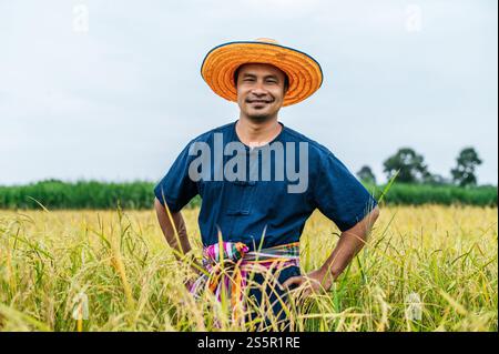 Portrait junger gutaussehender Bauer auf dem Reisfeld, er trägt Strohhut, er lächelt und steht auf der Taille und sieht in die Kamera Stockfoto