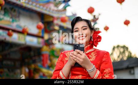 Porträt Asiatische schöne Frau mit einem Cheongsam lächelnd und mit Smartphone am Schrein am chinesischen Neujahr, Kopierraum Stockfoto