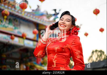 Porträt Asiatische schöne Frau mit einem Cheongsam lächelnd und mit Smartphone am Schrein am chinesischen Neujahr, Kopierraum Stockfoto