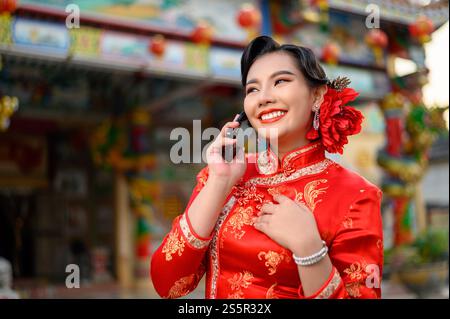 Porträt Asiatische schöne Frau mit einem Cheongsam lächelnd und mit Smartphone am Schrein am chinesischen Neujahr, Kopierraum Stockfoto