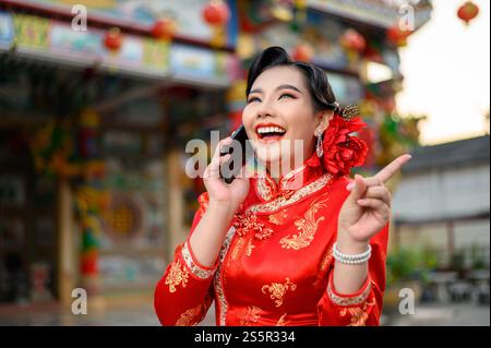 Porträt Asiatische schöne Frau mit einem Cheongsam lächelnd und mit Smartphone am Schrein am chinesischen Neujahr, Kopierraum Stockfoto