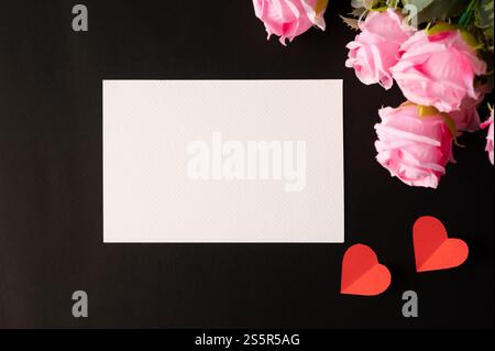 Weißes Papier und rosafarbene Blumen auf schwarzem Hintergrund Stockfoto