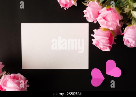 Weißes Papier und rosafarbene Blumen auf schwarzem Hintergrund Stockfoto