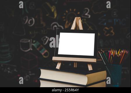 Schwarzer Fotorahmen auf dem Stand auf den Büchern im Klassenzimmer und Buntstifte Stockfoto