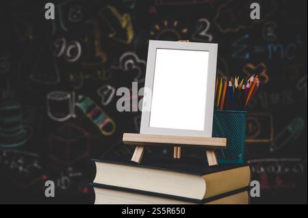 Weißer Fotorahmen auf dem Stand und Buntstifte auf den Büchern im Klassenzimmer Stockfoto