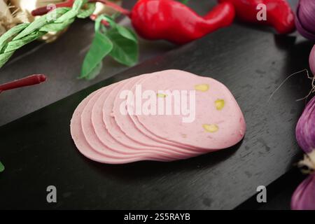 Rosafarbener Schinken mit grüner Paprika, kunstvoll auf einem Holzbrett angeordnet Stockfoto