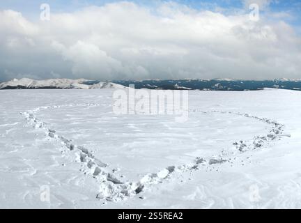 Menschlichen Fußabdruck bilden die Herzform auf schneebedeckten Berg-Plateau und Bergketten hinter. Stockfoto