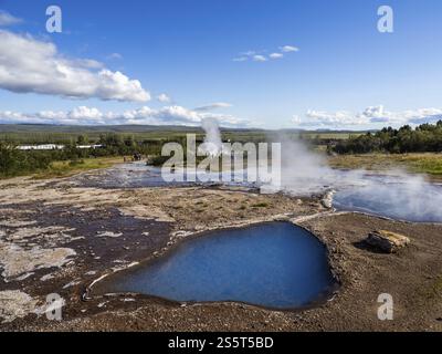 Heiße Quellen, Hochtemperaturgebiet im Haukadalur-Tal, Blesi-Thermalquelle vor dem Haus, Strokkur-Geysir, der dahinter ausbricht, Golden Circle Route, Island Stockfoto