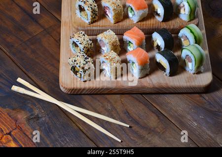 Eine detaillierte Aufnahme eines Satzes japanischer Sushi-Rollen und einer Vorrichtung für ihre Verwendung (Essstäbchen), die sich auf einem hölzernen Schneidebrett auf einem Tisch in befinden Stockfoto