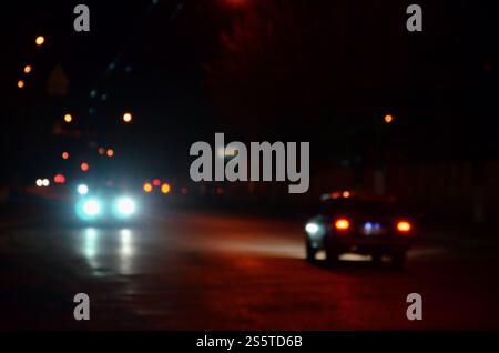 Unscharfe Verkehrslichter auf einer nassen regnerischen Stadtstraße bei Nacht - Pendeln zur Rush Hour Konzept abstraktes Bokeh von der Verkehrsbeleuchtung auf dem Verkehr Stockfoto
