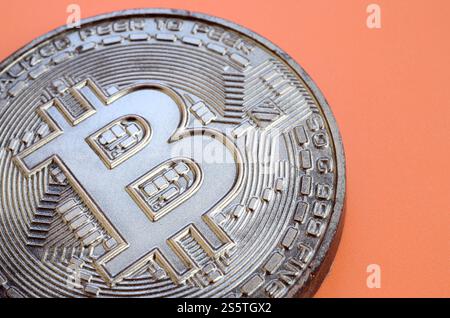 Schokoladenprodukt in Form von Bitcoin liegt auf einem orangefarbenen Kunststoffhintergrund. Modell der Kryptowährung in essbarer Form Stockfoto