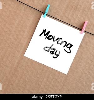 Beweglicher Tag. Die Notiz ist auf einem weißen Aufkleber geschrieben, der mit einem Kleiderschrank an einem Seil auf einem Hintergrund aus braunem Karton hängt Stockfoto