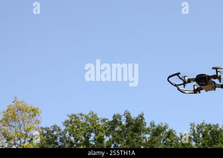 Drohne mit Fotokamera startet vom Land und fliegt für Luftaufnahmen am Sonnenuntergang Abend vor Bäumen. Drohne mit Fotokamera ab Stockfoto