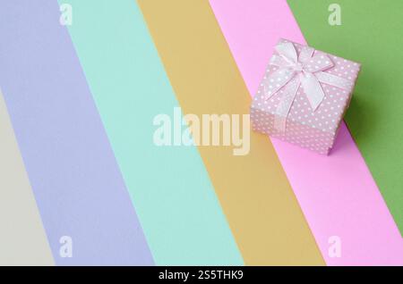 Kleine rosa Geschenkkarton liegen auf Textur Hintergrund der Mode Pastell rosa, blau, grün, gelb, violett und beige Papier in minimalen Begriff. Zusammenfassung Stockfoto