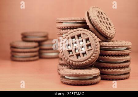 Ein Haufen Schokoladenkekse, gefüllt mit weißer Vanillecreme, liegt auf einer braunen hölzernen Oberfläche. Süße und leckere Sandwiches, runde Kekse. Detailliertes Essen Stockfoto