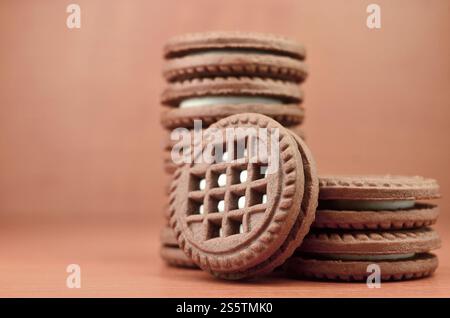 Ein Haufen Schokoladenkekse, gefüllt mit weißer Vanillecreme, liegt auf einer braunen hölzernen Oberfläche. Süße und leckere Sandwiches, runde Kekse. Detailliertes Essen Stockfoto