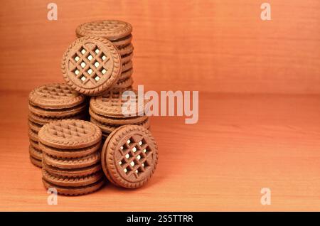 Ein Haufen Schokoladenkekse, gefüllt mit weißer Vanillecreme, liegt auf einer braunen hölzernen Oberfläche. Süße und leckere Sandwiches, runde Kekse. Detailliertes Essen Stockfoto