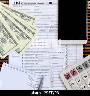 Zusammensetzung der Gegenstände, die auf dem Steuerformular 1040 liegen. Dollarscheine, Stift, Rechner, Smartphone, Büroklammer und Notizblock. Die Zeit, Steuern zu zahlen Stockfoto