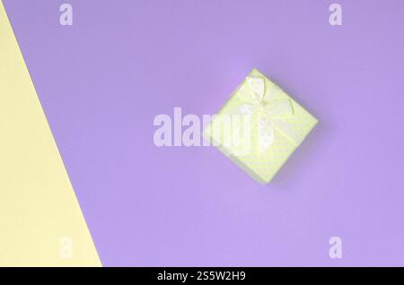 Kleine gelbe Geschenkbox liegt auf Textur Hintergrund von Mode Pastellgelb und violett Farben Papier in minimalem Konzept. Kleine gelbe Geschenkbox liegt drauf Stockfoto