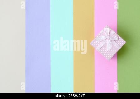 Kleine rosa Geschenkkarton liegen auf Textur Hintergrund der Mode Pastell rosa, blau, grün, gelb, violett und beige Papier in minimalen Begriff. Zusammenfassung Stockfoto