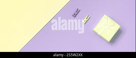 Kleine gelbe Geschenkbox und zwei Stifte liegen auf Textur Hintergrund von Mode pastellgelb und violett Farben Papier in minimalem Konzept. Kleines gelbes Geschenk Stockfoto