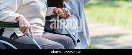 Asiatische Seniorin im Rollstuhl mit glücklicher Tochter. Familienbeziehung Rentnerin sitzend auf Rollstuhl in der Parkalpflege im Altersheim Stockfoto