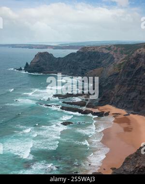 Sandstrand mit felsigen Bergrücken trübes Wetter Aussicht auf Sommer Atlantic an der felsigen Küste (Costa Vicentina, Algarve, Portugal). Und Ocean Surf Wellen. Stockfoto