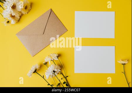 Leere Karte mit Umschlag und Blume ist auf gelbem Hintergrund platziert Stockfoto