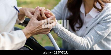 Asiatische Seniorin im Rollstuhl mit glücklicher Tochter. Familienbeziehung Rentnerin sitzend auf Rollstuhl in der Parkalpflege im Altersheim Stockfoto
